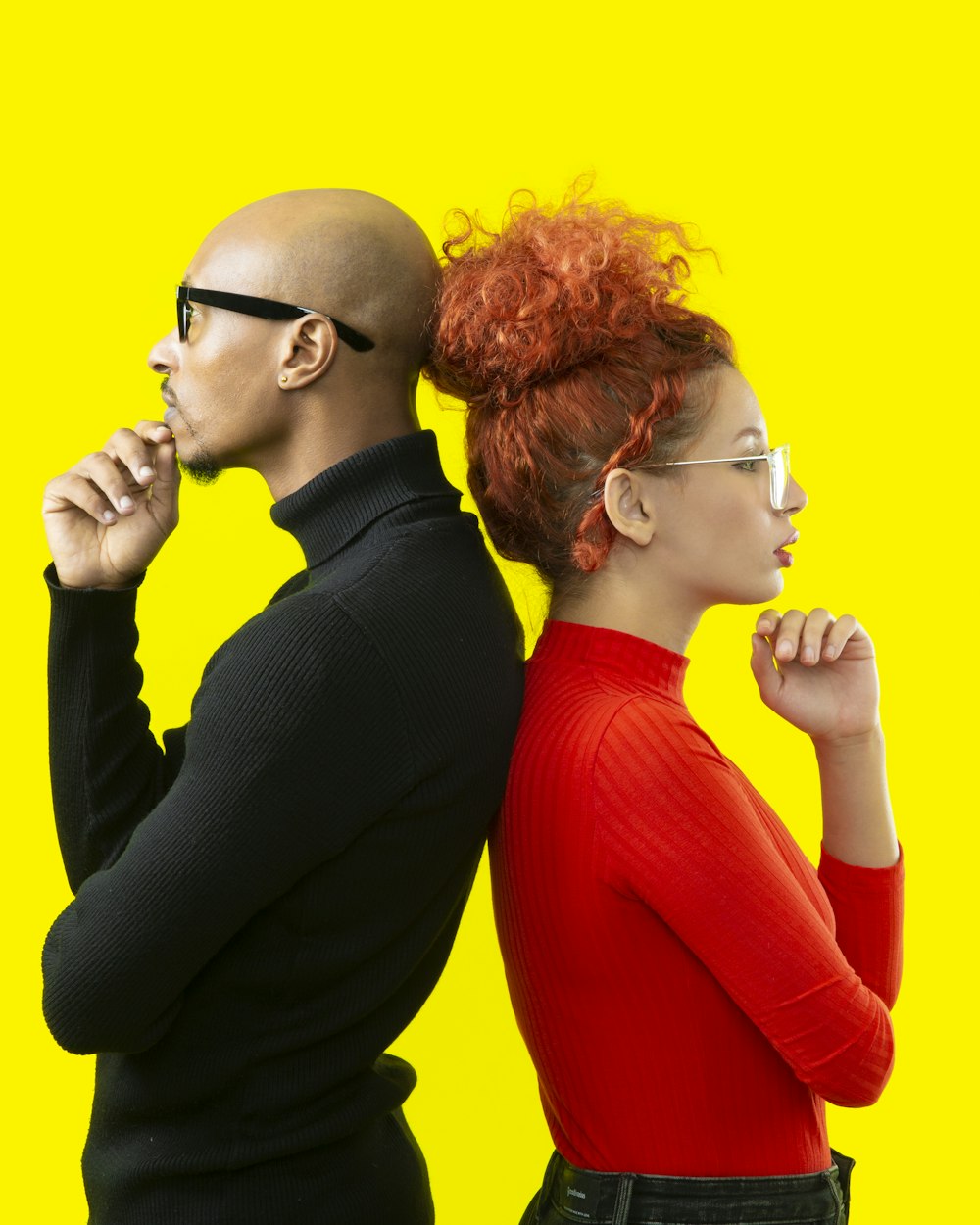 A smiling couple in glasses against a sunny yellow wall