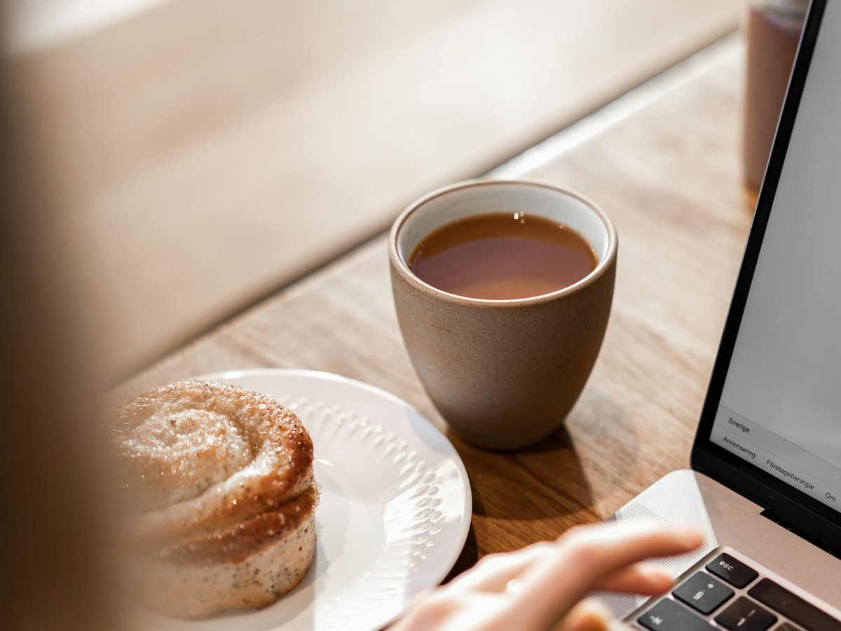 A cup of tea and a pastry beside an open laptop